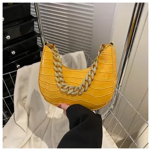 Detalle de bolso de mano amarillo con efecto cocodrilo y correa de cadena brillante.