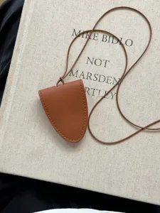 Gros plan d'un collier pendentif géométrique en cuir marron minimaliste avec petite poche.