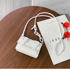 Close-up detail of white mini crossbody bag with buckle design, showcased on wooden table.