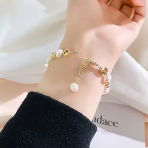 Close-up detail of elegant freshwater pearl and gold-tone metal bracelet on hand.