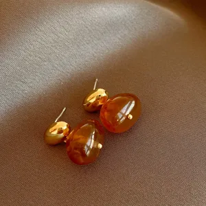Detailed close-up shot of retro brown resin and gold geometric stud earrings, glossy finish.