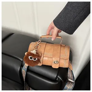 Sac à main cylindrique marron élégant avec fermoir pivotant, rivets et large sangle chic.