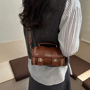 Sac bandoulière cylindrique marron chic avec sangle large, rivets rétro et fermoirs métalliques.