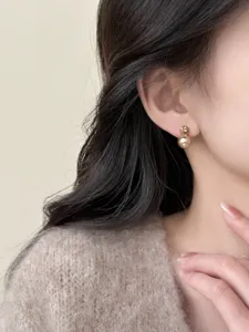 Close-up detail of elegant champagne pearl and zircon stud earrings worn by model.