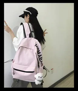 Pink school backpack detail view featuring side letter print and cute white bear pendant.