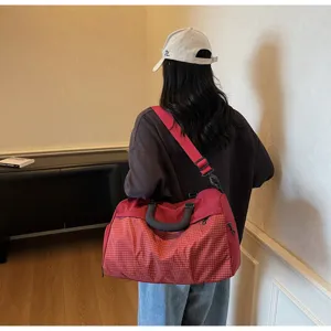 Detailed view of the red plaid travel gym bag showing shoulder strap and grid fabric texture.