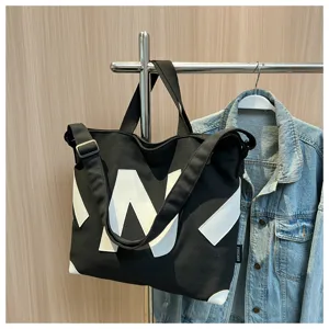 Black canvas tote bag detail featuring geometric white letters and corner patch reinforcement.