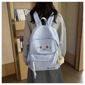 Detail view of light blue cute cartoon backpack featuring playful animal expression and plush charm.