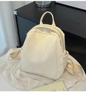 White leather backpack detail view showing front pocket design, smooth zipper and top handle.