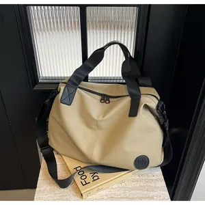 Detail view of casual khaki nylon travel duffel bag with black straps and logo patch.