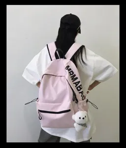 Detailed view showing the pink student backpack strap with lettering and bear pendant.