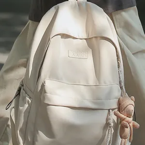 Minimalistischer beiger Rucksack fuer Studenten, laessige Schultueche mit niedlichem Baerenanhang.