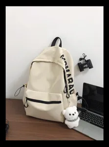 Beige canvas backpack detail featuring black zippers, side text, and a cute white bear pendant.