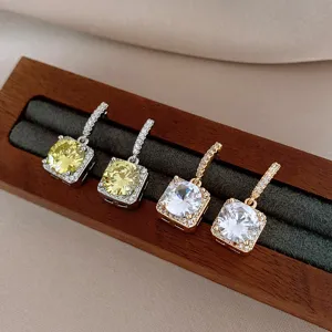 Detailopname van vierkante zirkoon oorbellen op houten standaard, elegant sieradenontwerp.