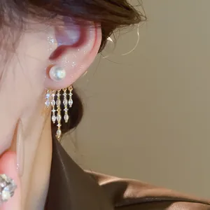 Close-up detail shot of elegant pearl and sparkling zircon tassel earrings in gold tone.