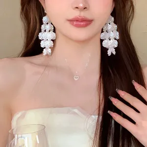 Detailed shot of elegant white petal tassel earrings and minimalist clear heart necklace set.
