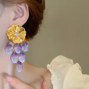 Close-up detail of gold flower purple gradient petal tassel earrings worn on ear.