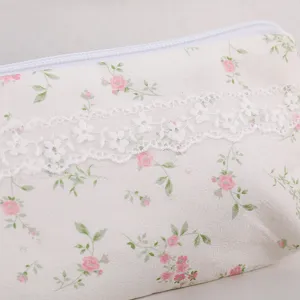 Dettaglio ravvicinato dell'astuccio floreale con delicati fiori rosa e bordo in pizzo bianco.
