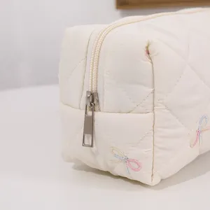 Close-up detail of quilted cosmetic bag featuring cute colorful bow embroidery and zipper.
