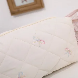 Close-up detail of quilted beige cosmetic pouch featuring colorful embroidered bows and zipper.