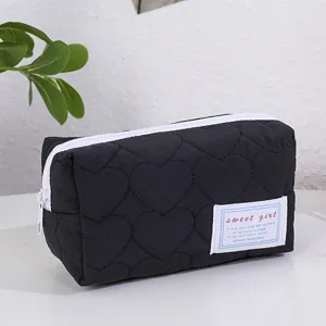 Détail de trousse de maquillage noire matelassée en cœur, pochette souple zippée blanche et étiquette.