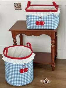 Blauer karierter Stoff-Aufbewahrungskorb mit Kirschen-Bestickung und Spitzenbesatz zu Hause.