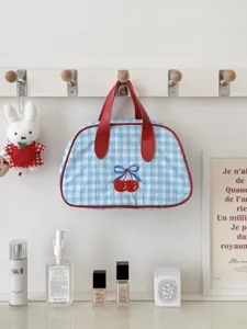 Close-up detail of the blue gingham cosmetic bag with red cherry embroidery and top handle.