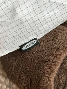 Close-up detail of white grid storage bag fabric with brand label and plush brown texture.