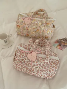 Dettaglio di borse da viaggio trapuntate floreali su uno sfondo di letto bianco morbido.