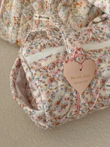 Dettaglio ravvicinato della borsa cilindrica trapuntata floreale con etichetta a cuore.