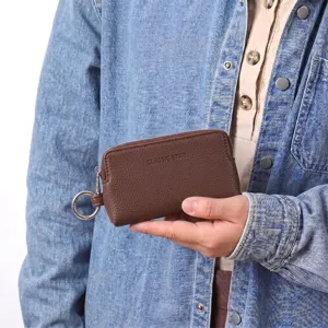 Gros plan détaillé du porte-monnaie à clés marron en cuir texturé avec anneau métallique.