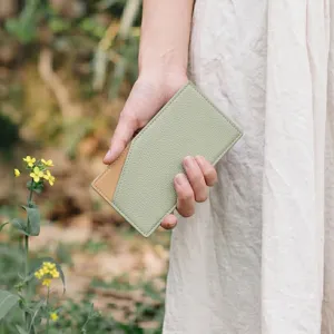 Detail view of minimalist leather card holder wallet held in hand, thin bi-fold design.
