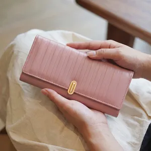 Vue détaillée d'un long portefeuille rose à rayures verticales et fermoir doré tenu par les mains.