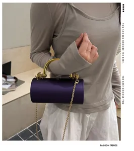 Vista dettagliata della borsa da sera cilindrica viola scuro con manico e catena dorati.