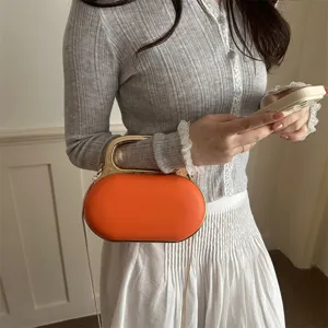 Close-up detail shot of the orange oval handbag featuring a metal handle and chain strap.