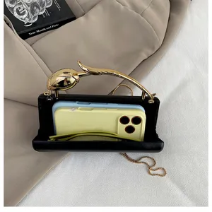 Detailopname van zwarte avondtas met gouden metalen tulphendel en ketting op stof.