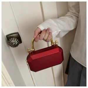 Detailed view of the red acrylic box evening bag with gold metal handle and chain strap.