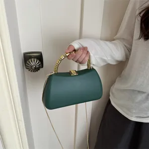 Detail shot of dark green hard shell clutch bag with gold metallic handle and chain strap.
