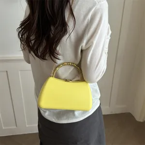 Detail view of yellow hardshell evening bag with metal bamboo ring handle and chain strap.