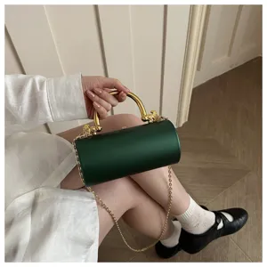 Dettaglio elegante della borsa da sera cilindrica verde scuro con manico dorato e catena.