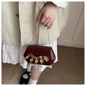 Detailansicht der weinroten Acryl-Clutch mit goldenem Metall-Hand-Dekor und funkelnden Steinen.