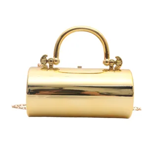 Dettaglio clutch da sera cilindrica dorata, elegante manico in metallo e tracolla a catena.