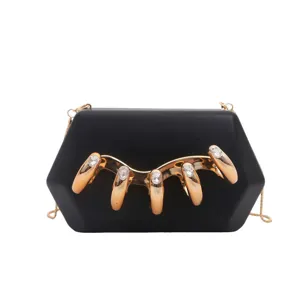 Details der schwarzen Acryl-Clutch mit goldener Metallklaue und funkelnden Strasssteinen.