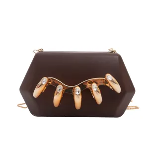Detailansicht der braunen Acryl-Clutch mit goldenem Krallen-Metall-Element und feinen Ziersteinen.