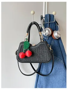 Sac à main en paille noire avec breloque cerise, poignées en cuir. Vue de détail chic.
