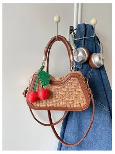Vue détaillée d'un sac en paille d'été avec bordure en cuir marron et charmant pendentif cerise.