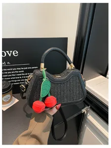 Gros plan sur le sac à main tressé noir avec pendentif cerise rouge et poignée en cuir.
