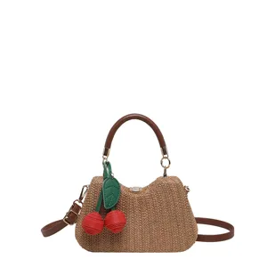 Gros plan détaillé du sac à main en paille tissée avec charmant cerise rouge et poignées.