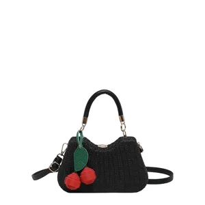Détail de sac bandoulière en paille noire avec charmant pendentif cerise pour plage été.