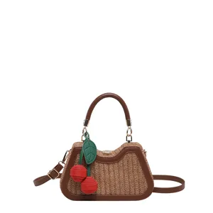 Détail en gros plan du sac à main en paille tissée avec une breloque cerise rouge et cuir.